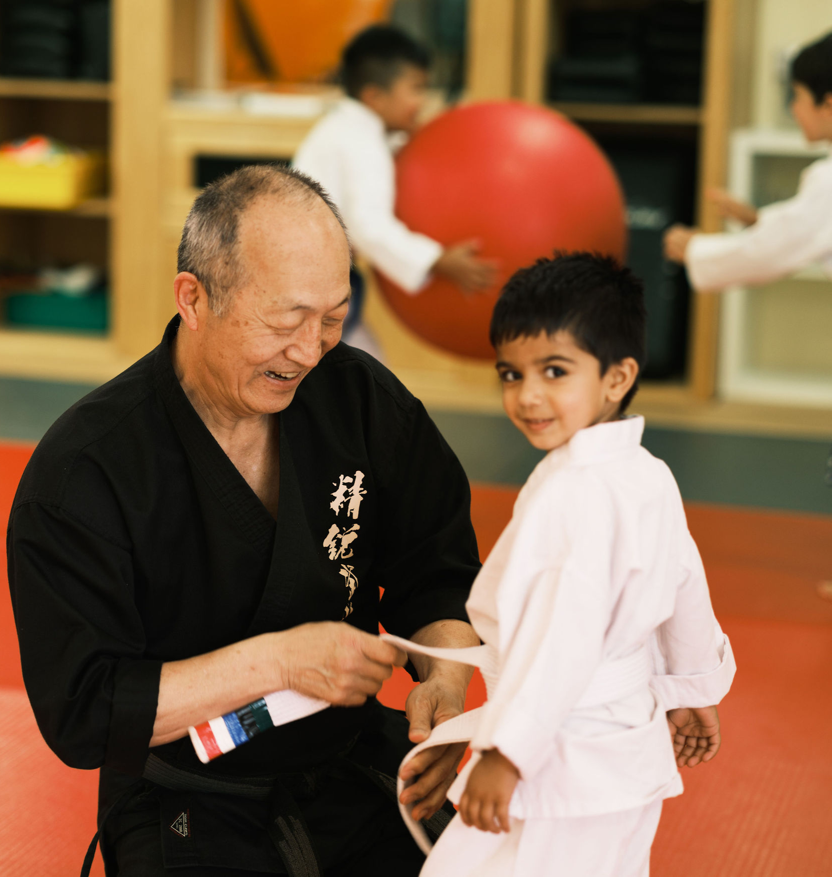 Master Kim tying a white belt on a smiling young student